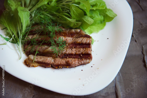 grilled piece of pork with fresh greeny on the white plate