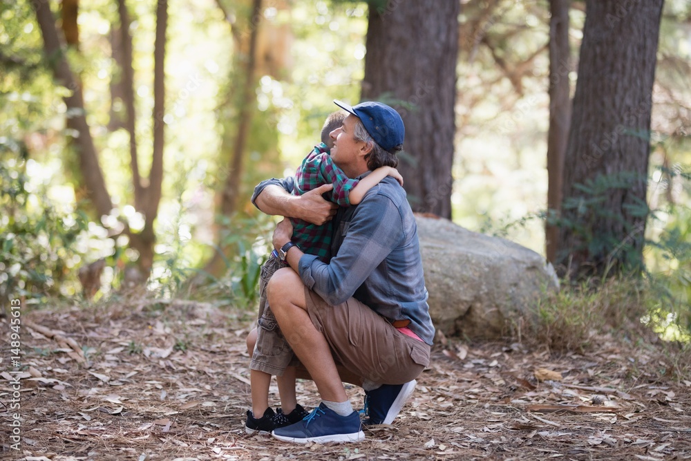Father and son embracing while hiking in forest