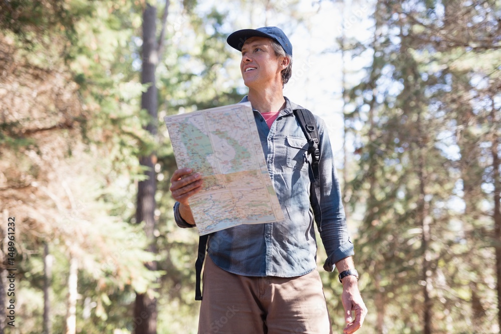 Low angle view of hiker with map standing in forest Low angle view of hiker with map standing in forest
