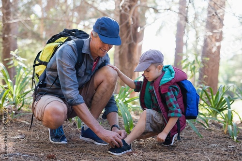 Father tying shoelace for son in forest