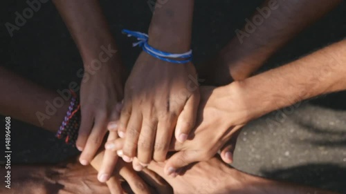 Arm of all races and colors stacked together one by one in unity and teamwork and then raised. Many multiracial hands getting together in the center of a circle and then cheer. Close up outdoor shot