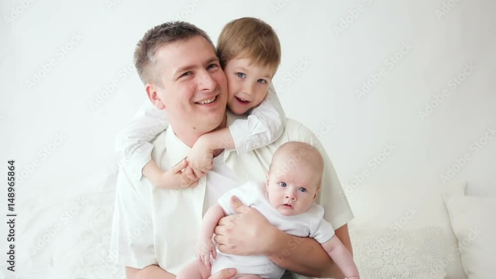 father with two sons sitting at home on a white bed father with two sons sitting at home on a white bed