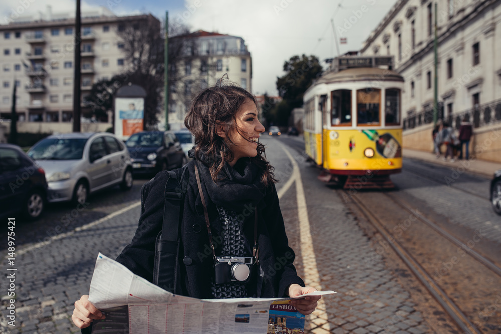 Admiring amazing trip in european metropola.Traveling in Europe.Female turist in front of  famous 28 tram in Lisbon,Portugal.Woman holding maps and exploring charming country