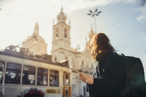 Admiring amazig sunset in european metropola.Traveling in Europe.Female turist in front of Basilica da Estrella and famous 28 tram in Lisbon,Portugal.Woman holding maps and exploring charming country