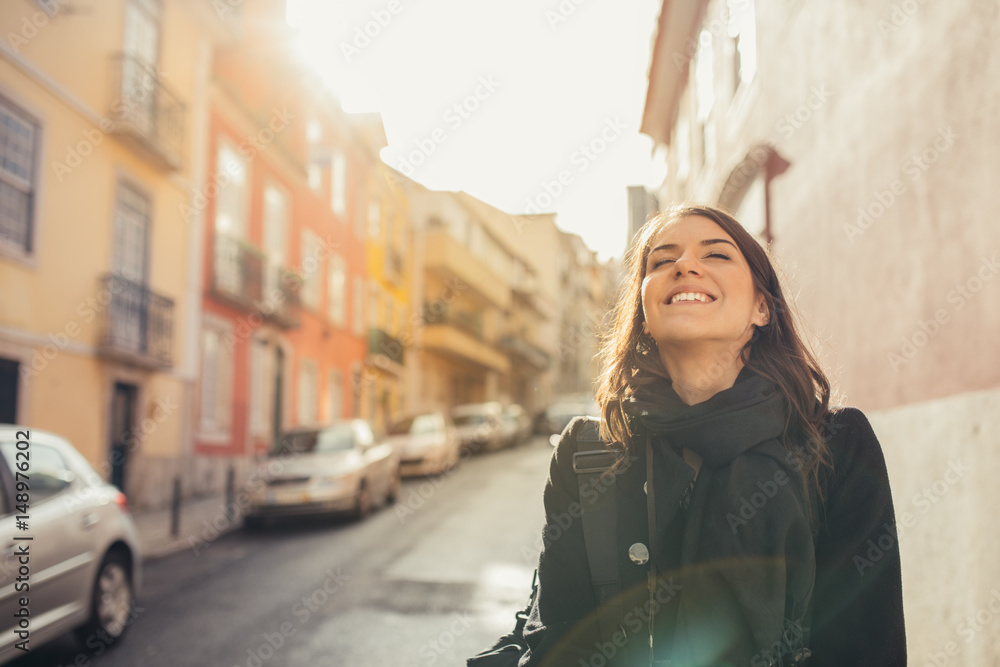 Enjoying beautiful warm and sunny day in Lisbon, Portugal.Sunset sun rays in small narrow street of colorful Lisbon.Experiencing charming european city.Smiling woman admiring Lisbon architecture
