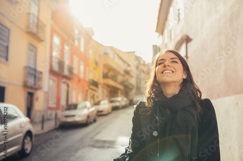 Enjoying beautiful warm and sunny day in Lisbon, Portugal.Sunset sun rays in small narrow street of colorful Lisbon.Experiencing charming european city.Smiling woman admiring Lisbon architecture photo