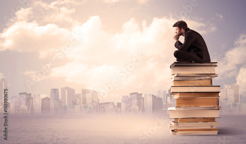Man sitting on pile of books above city