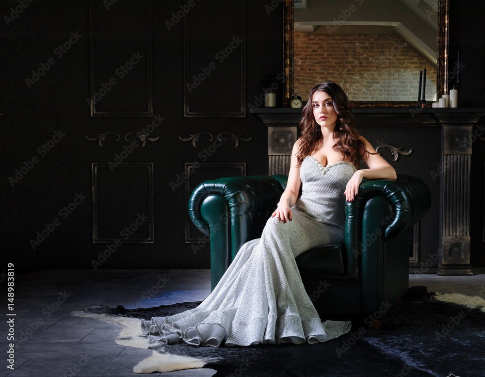 beautiful woman in evening dress sitting on a leather armchair in a ...