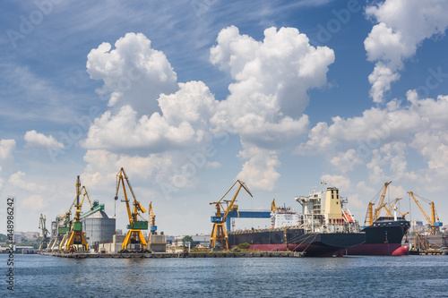 Scenic view with cumulus clouds above industrial seaport with large freighters docked for shipping in Constanta, Romania.