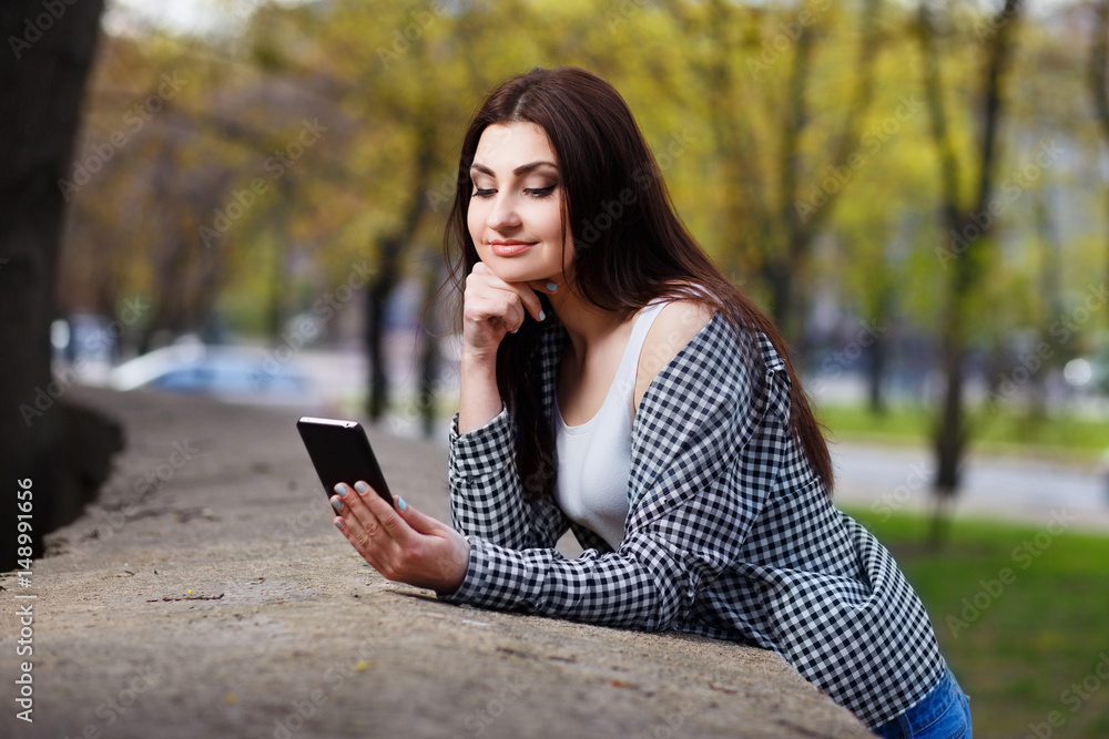 Obraz premium Young pretty stylish woman talking on smart phone in the city park