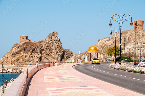 Ulica i deptak wzdłuż wybrzeża w Muscat z widokiem na ruiny fortów na skale. 