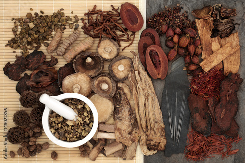 Traditional chinese herbal medicine selection with acupuncture needles and mortar and pestle forming a background. photo