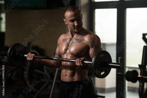 Bodybuilder Exercising Biceps With Barbell In Gym