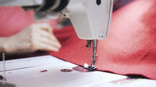 Close up of woman s hands sewing red fabric at a sewing machine and cutting excessive material with scissors. Locked down real time close up shot photo