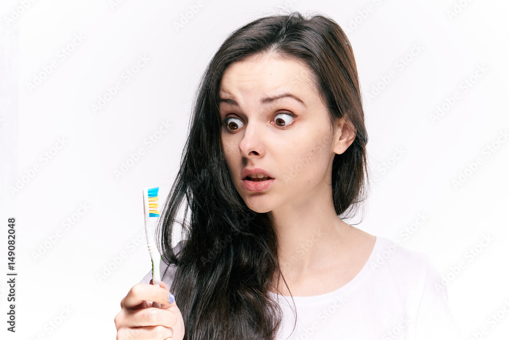 woman with surprise looks at blue toothbrush, light background woman with surprise looks at blue toothbrush, light background