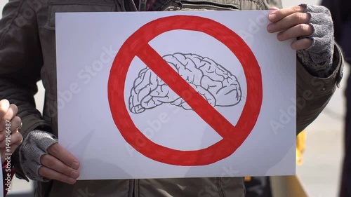 Red strikethrough notice above the figure of the brain - Sign of prohibition, denial and restriction. The boy holds a sign or banner with the image of a person's stupidity. photo