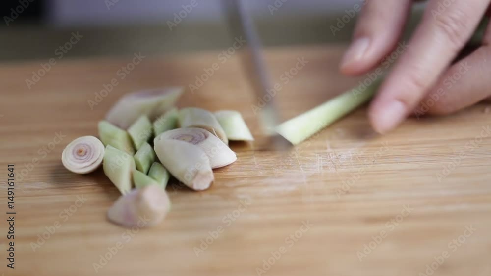 A female hand slicing lemongrass on bamboo wooden plate with other Thai herbs beside. A female hand slicing lemongrass on bamboo wooden plate with other Thai herbs beside.