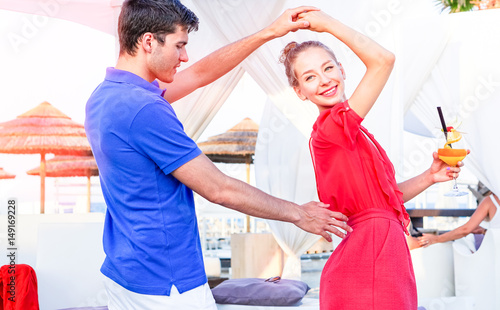  Attractive young couple dancing at sunset on the beach resort - Happy lovers having fun at cocktail party on holiday - Concept of summer vacation happy moments