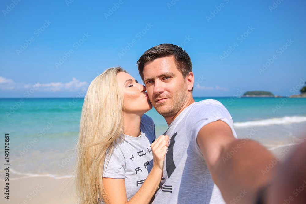 Outdoor closeup portrait of pretty young couple in love takes a self-ie having fun in hot weather and feeling happy together on the tropical island. Posing and hugs alone on the beach.