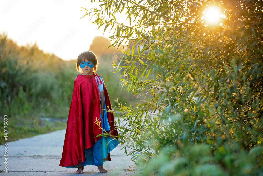 Cute sweet little preschool child, boy, playing superhero on a rural path in a small village
