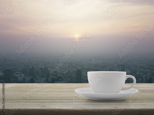 White coffee cup on wooden table over city tower at sunset, vintage style