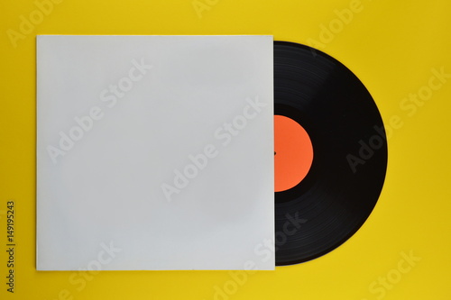 old black vinyl record with blank orange label halfway out of its white blank cover on yellow background 