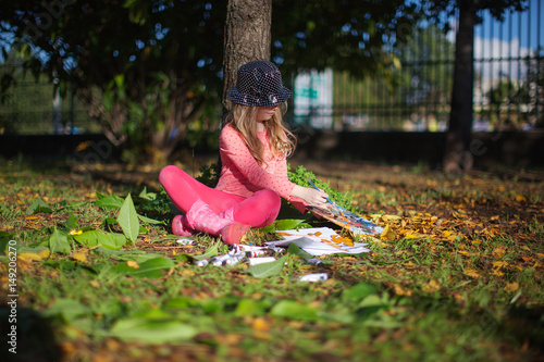 Little girl in the park under the autumn maple trees and drawing images