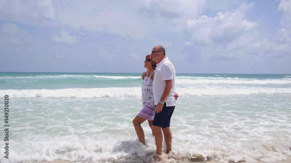 Middle-Aged Couple Walking On Tropical Beach in Sea Waves Middle-Aged Couple Walking On Tropical Beach in Sea Waves