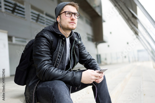 Modern young man listening to music with mobile phone in the street.