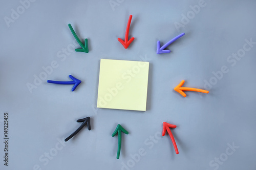 Input text idea: Top view of colorful arrow and yellow sticky note on grey background, business outside in concept