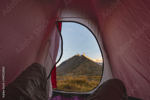 Camping with tent on the Alps. View from tent interior at sunrise, body part. Adventure and exploration, outdoor activity.