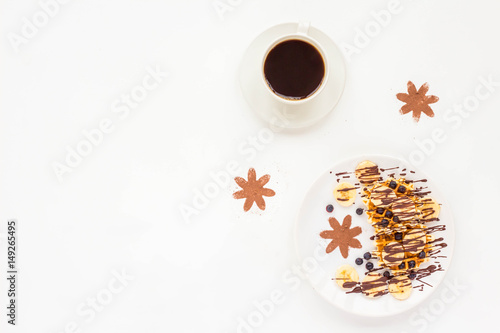Breakfast with pate of belgian waffles with fresh fruit, chocolate, banana, berry, blueberries, cup of black coffee on white background. Flat lay, top view, mock up photo