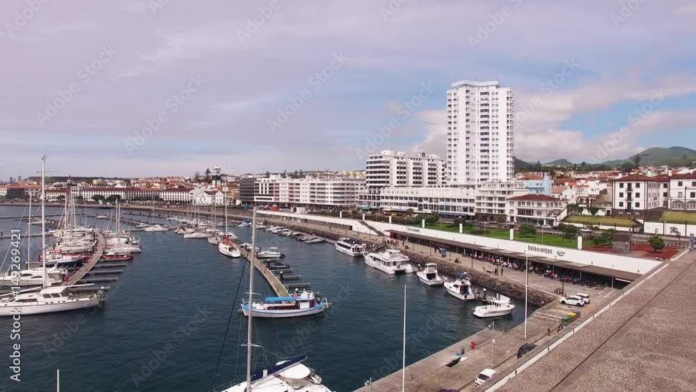 A view on Ponta Delgada from marina, Sao Miguel, Azores, Portugal. Moored yachts and boats along the port piers on a beautiful morning. A view on Ponta Delgada from marina, Sao Miguel, Azores, Portugal. Moored yachts and boats along the port piers on a beautiful morning.