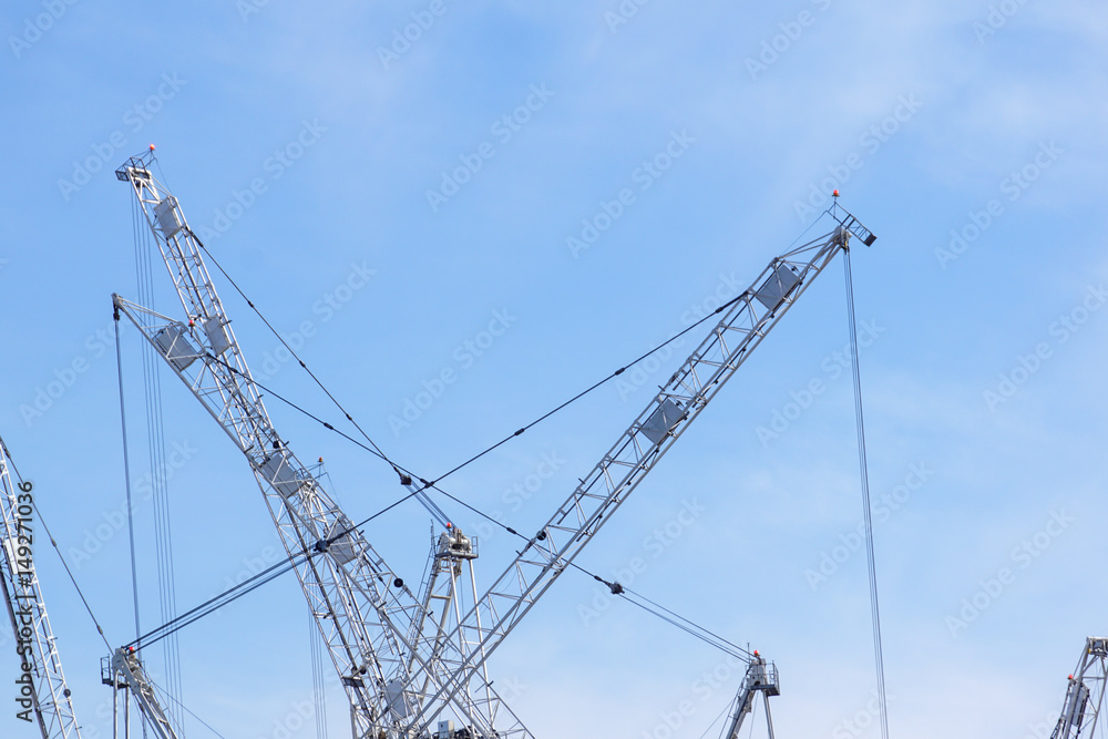 Tall white tower crane detail against bright blue sky. Tall white tower crane detail against bright blue sky.