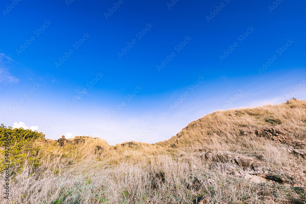 Beautiful rocks mountain lanscape and dry meadow in bright blue sky