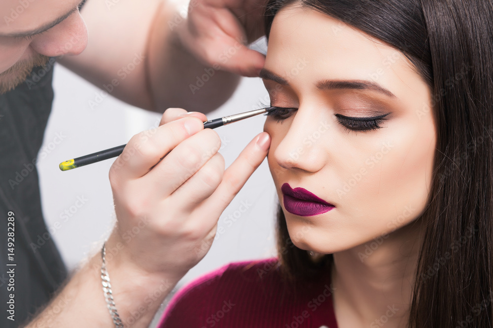 Male make-up artist Paints eyelids to brunette girl in beauty salon, close up Male make-up artist Paints eyelids to brunette girl in beauty salon, close up