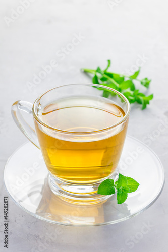 Herbal mint tea in a glass cup with fresh peppermint on background, vertical