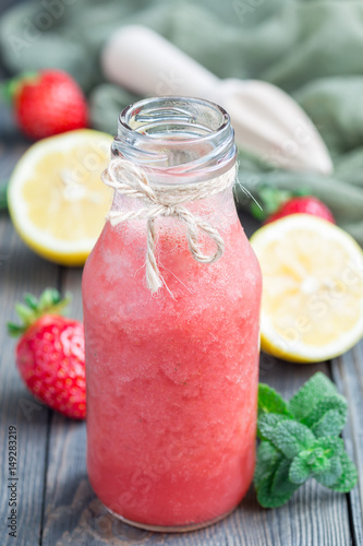 Homemade blended lemonade with fresh strawberry, lemon, ice and mint in glass bottle, vertical