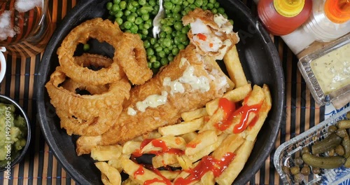 Dolly top down view of an English fish and chips with garden peas, ring onions and mushy peas