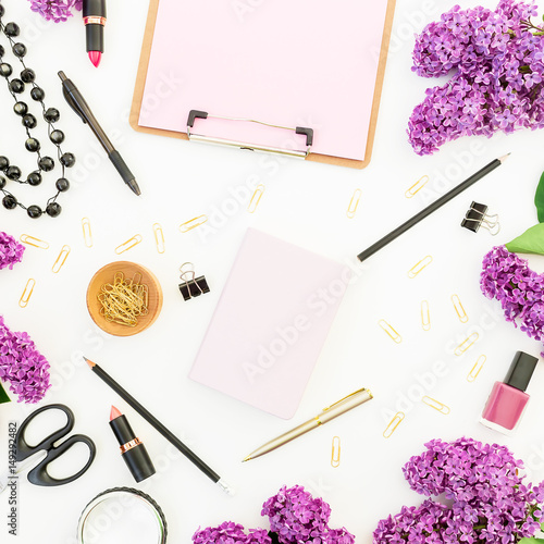 Blogger or freelancer workspace with clipboard, notebook, cosmetics, branches of lilac and accessories on white background. Flat lay, top view. Beauty blog concept.