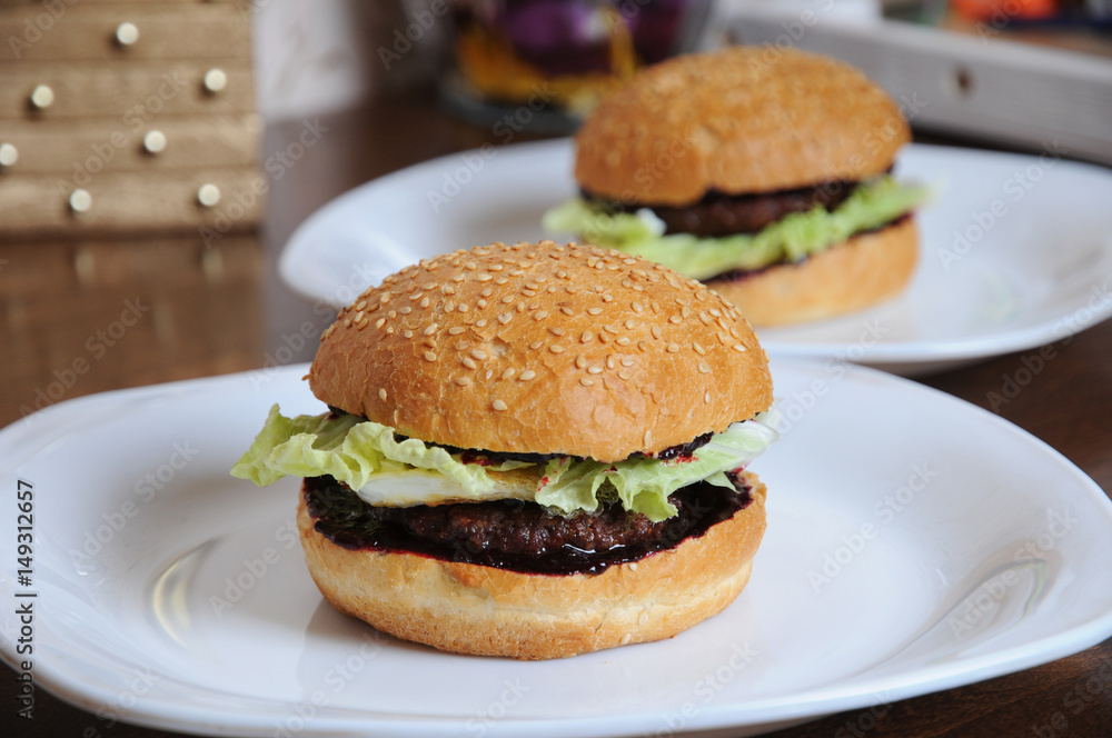 Two burgers with berry sauce on white plates Two burgers with berry sauce on white plates