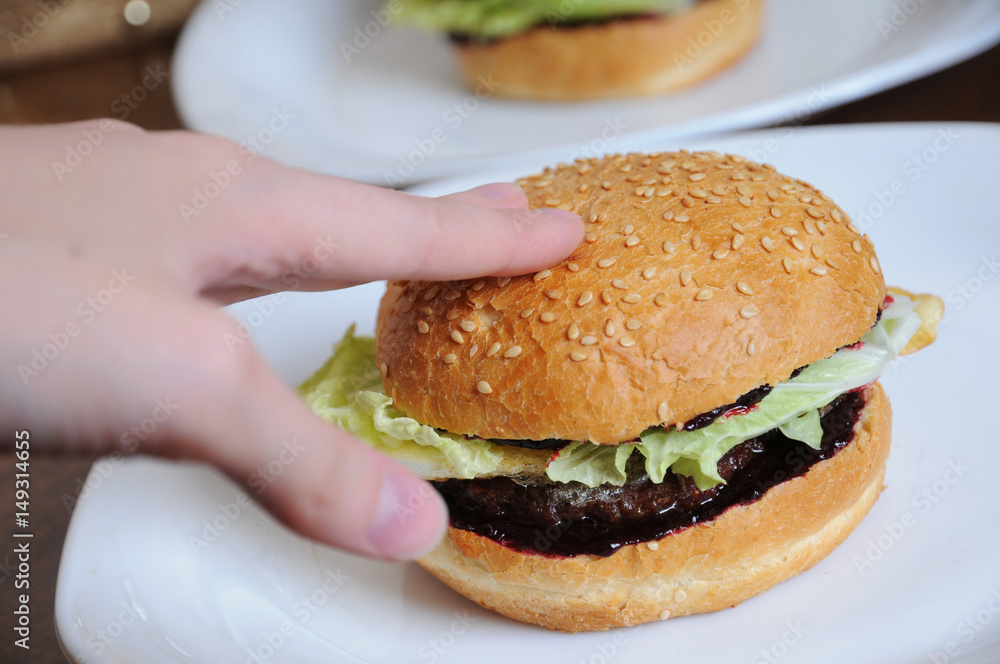 Burger with greens in hand on a white plate Burger with greens in hand on a white plate
