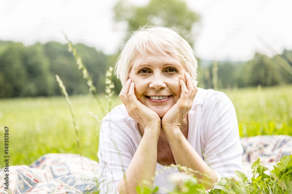 Senior woman lying on grass with hands on chin Senior woman lying on grass with hands on chin