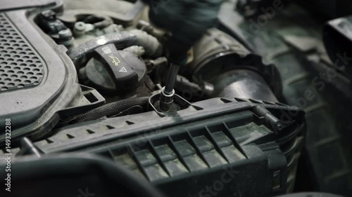 Mechanic twists fastening bolt on case of air filter. Man works in black special gloves. Filtration element settles down in front part of motor compartment near valvate cap of head of the cylinder photo