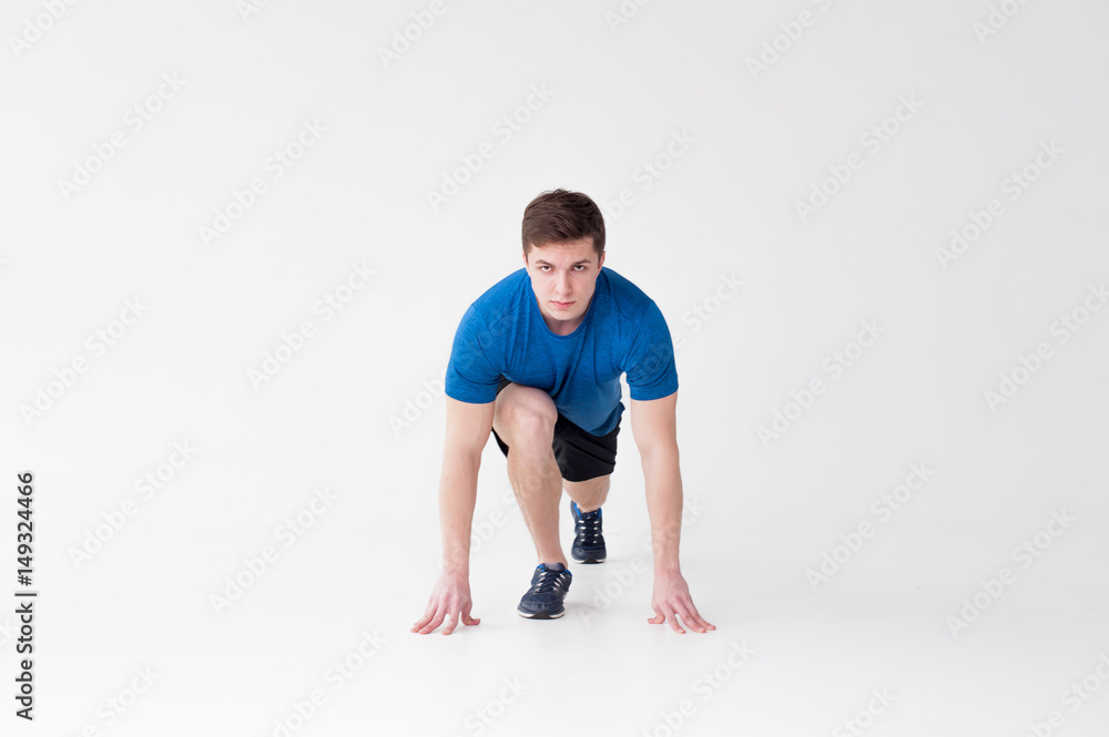 Running man on low start. Stands in rack, ready to achieve goals and wins. Young sexy Muscular male athlete wearing sporty blue t-shirt and shorts, studio portrait white background.Motivation concept