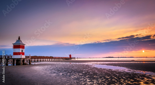 Beautiful sunrise at the seaside in Italy, at Lignano Sabbiadoro, with pier and lighthouse in the foreground.