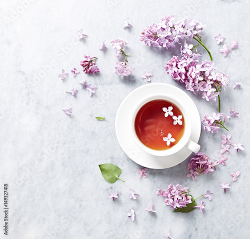 Cup of tea with lilac flowers on marble background