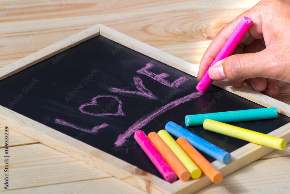 Obraz premium A colorful pastel crayons, a white paper and a hand writing an inscription 