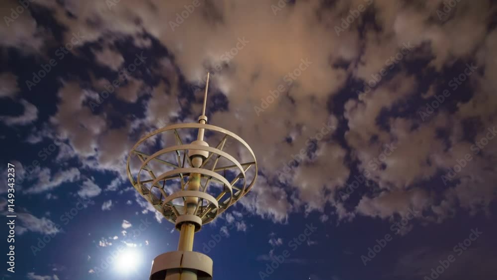 Building spire set against timelapse moon with flowing clouds.