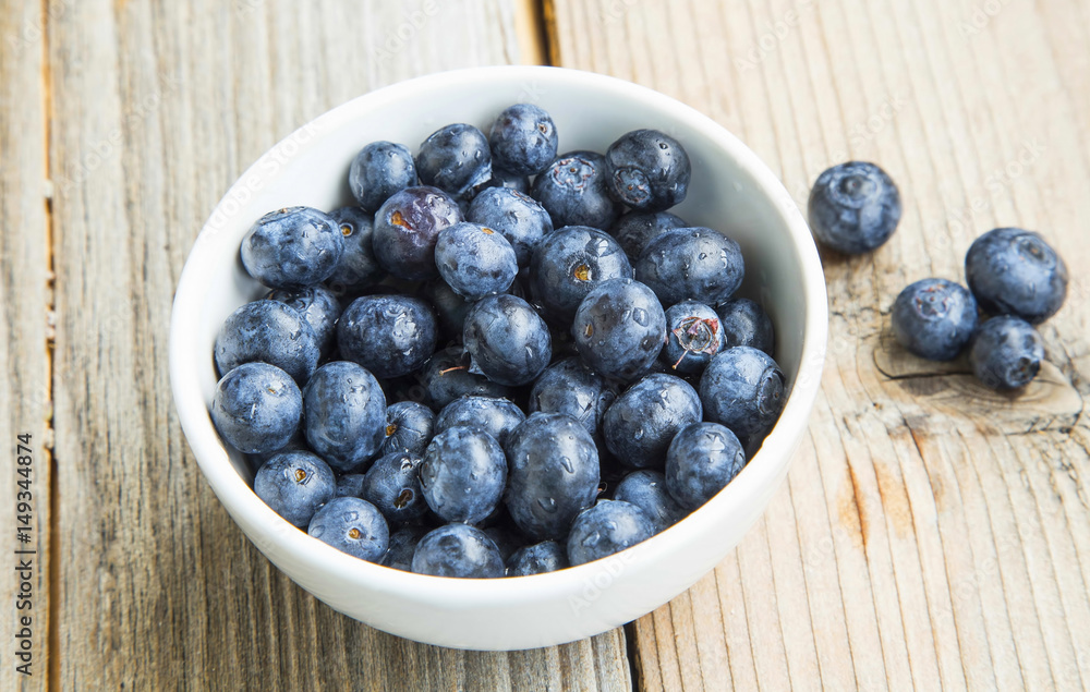 Blueberries in a bowl, healthy berry fruits in white bowl on wooden background Blueberries in a bowl, healthy berry fruits in white bowl on wooden background